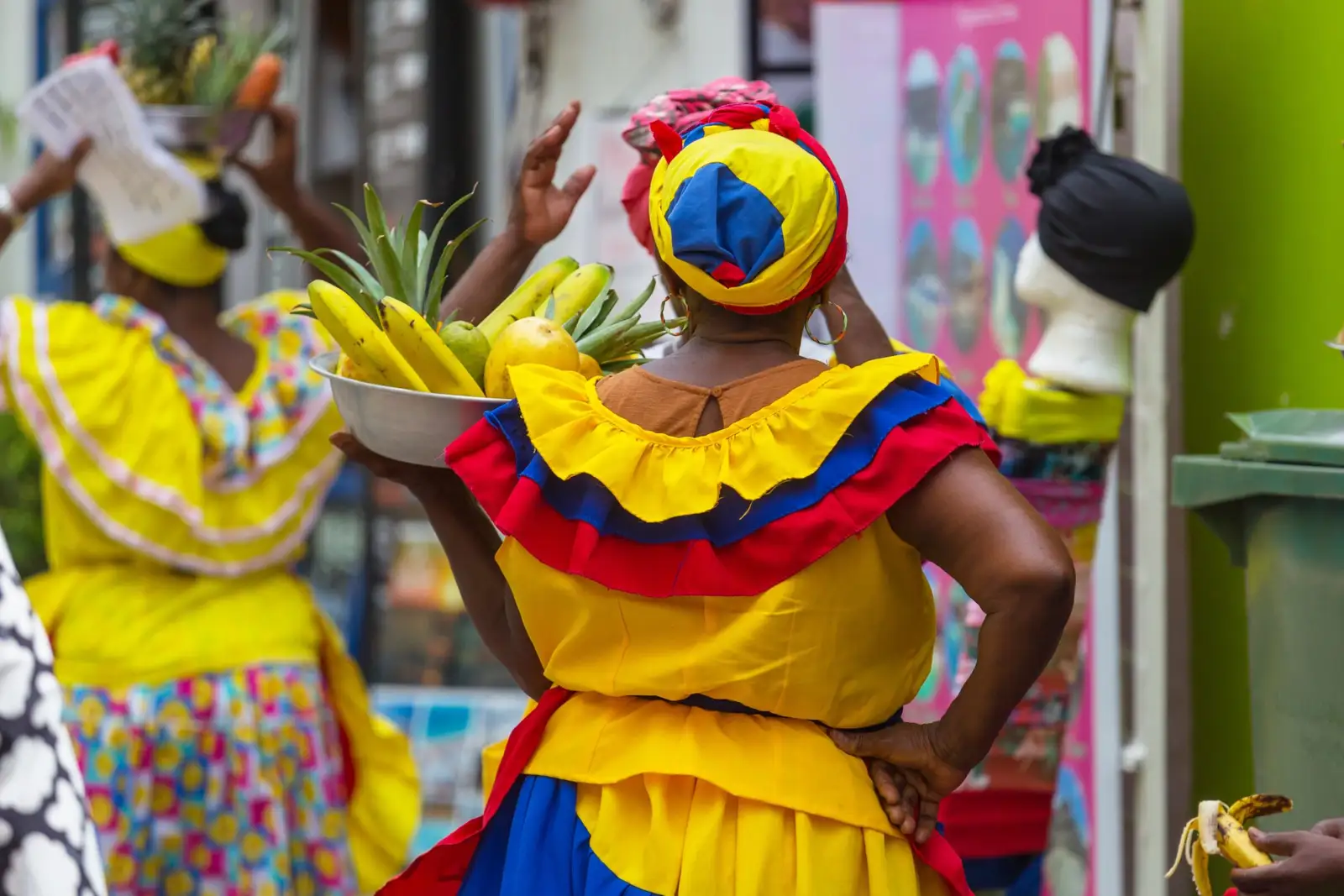 Palenqueras in yellow, blue and red dresses carrying bowls of fruit