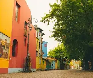 An orange building with a mural, on a street of painted houses in La Boca
