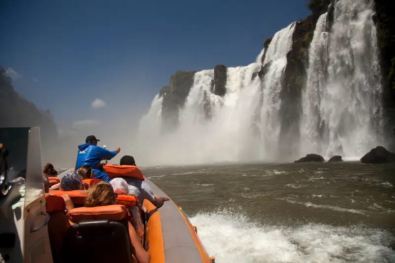 A boat of passengers in life jackets at the base of a waterfall