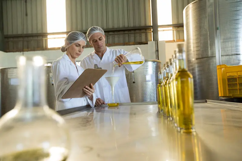 Two winery staff in white coats checking bottles in the cellar