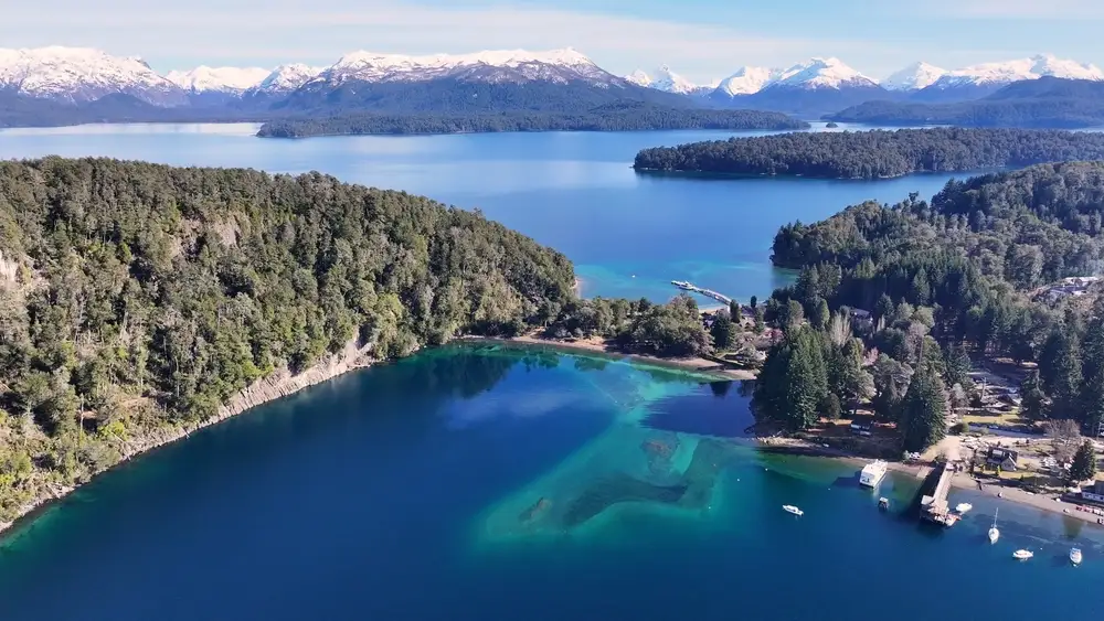 A lake and its wooded shore from above, with snow peaks beyond