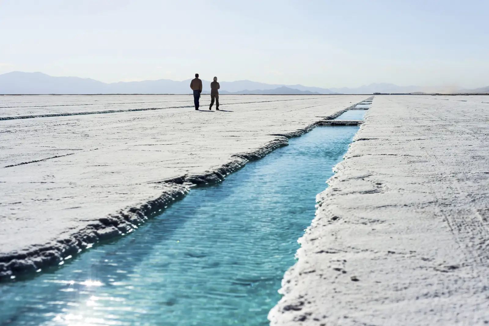 Two people on the salt flats beside a water channel