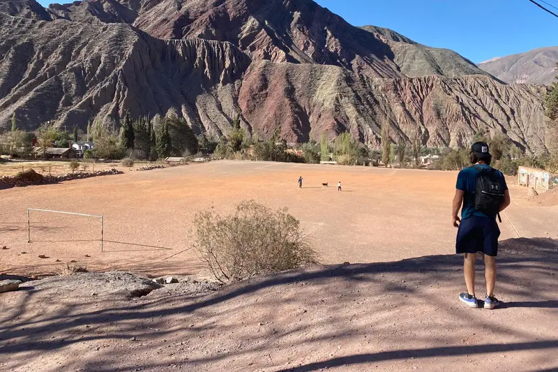 A walker on the desert floor below a wall of banded rock
