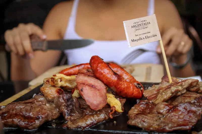 Grilled beef and sausages on a board, with an Argentine flag pick