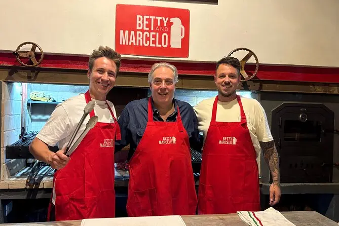 Three guests in red aprons by the asador oven