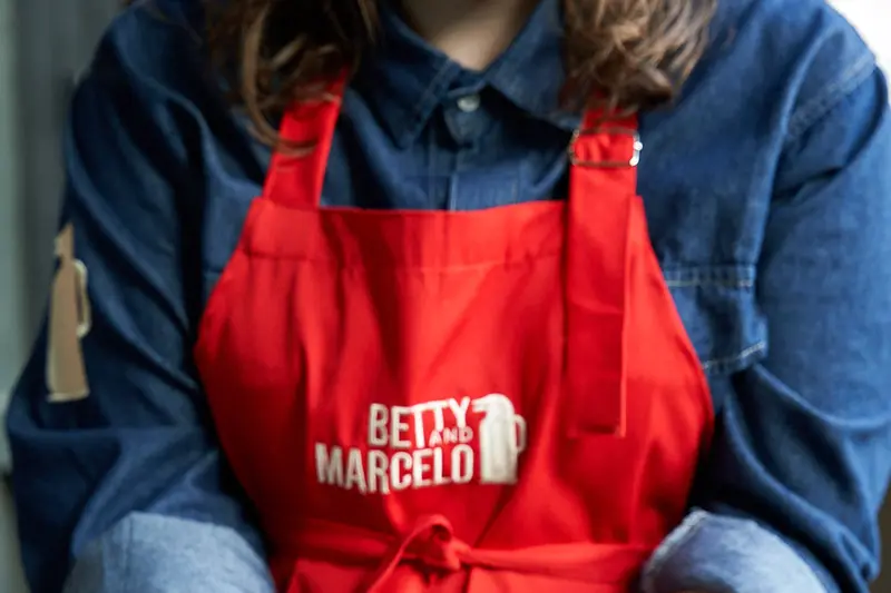 Hands holding a tray of chimichurri toast, wearing a Betty and Marcelo apron