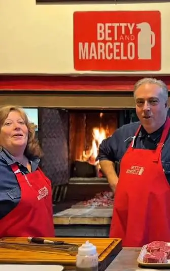 Betty and Marcelo standing by the lit asador fire