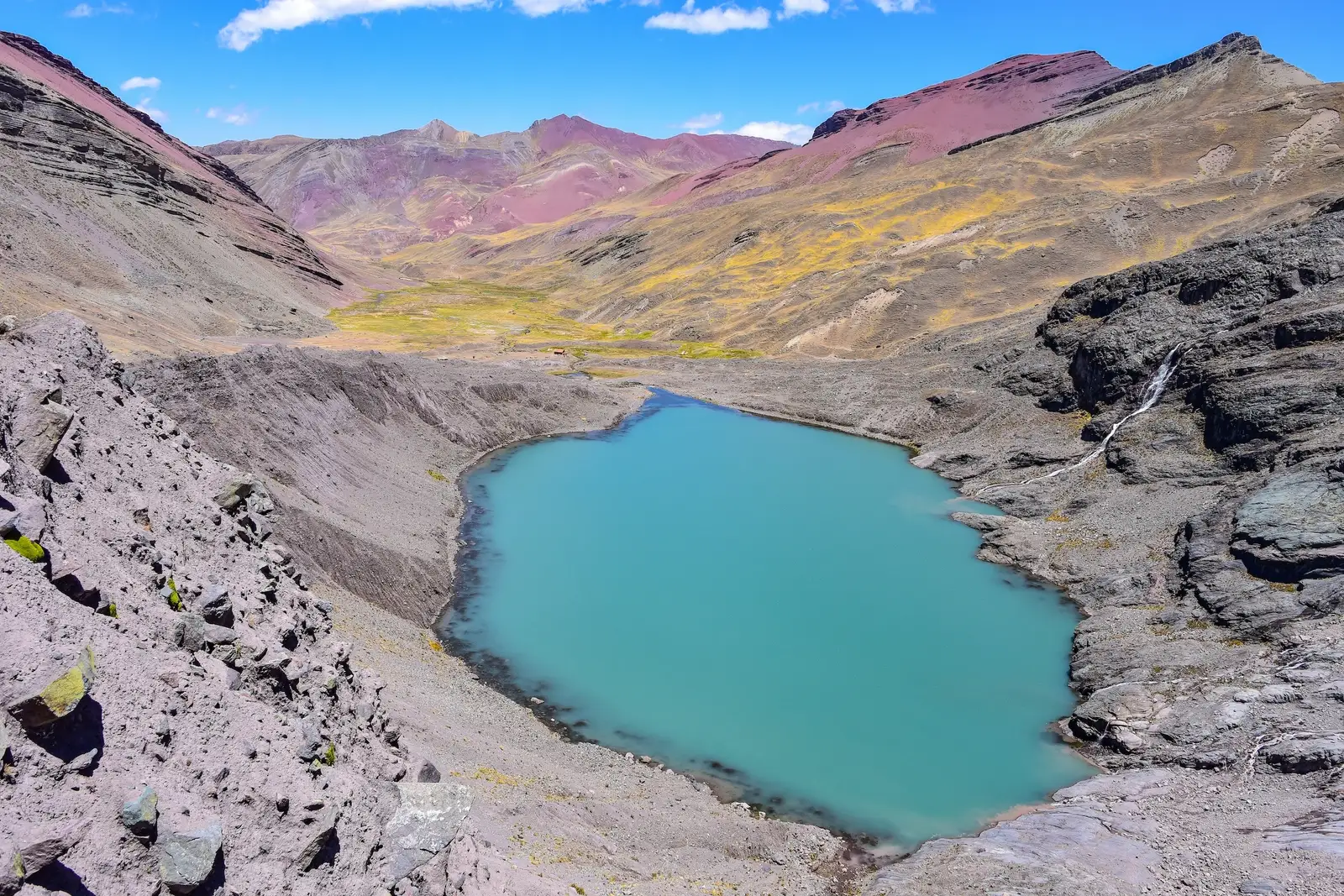 A turquoise lake below red and yellow mountains