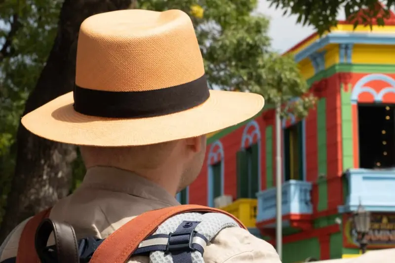 A visitor in a straw hat in front of the painted houses of Caminito