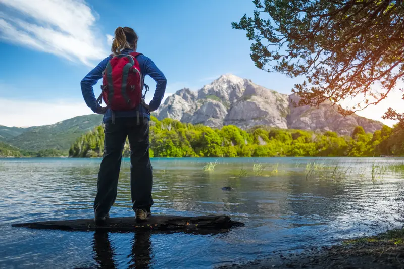 A walker standing on a rock, looking out at the lake and the peaks