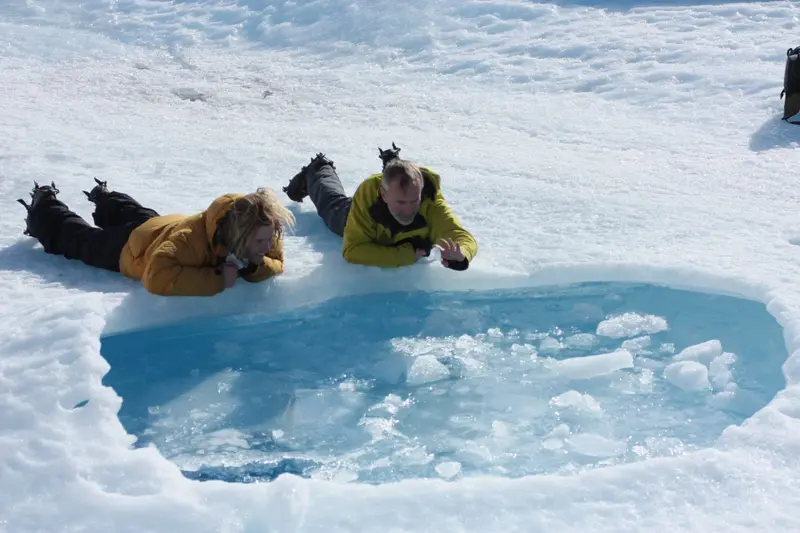 Two people lying at the edge of a meltwater pool on the ice