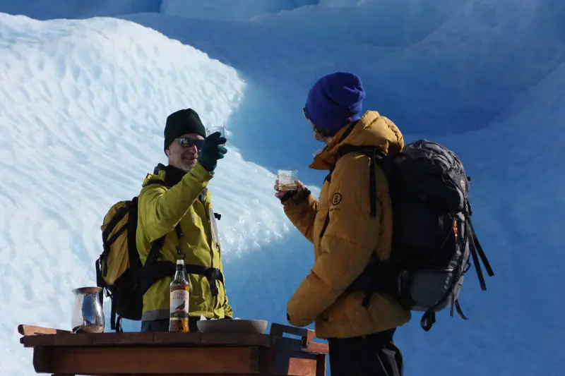 Two guides with a small table and a bottle set up on the ice