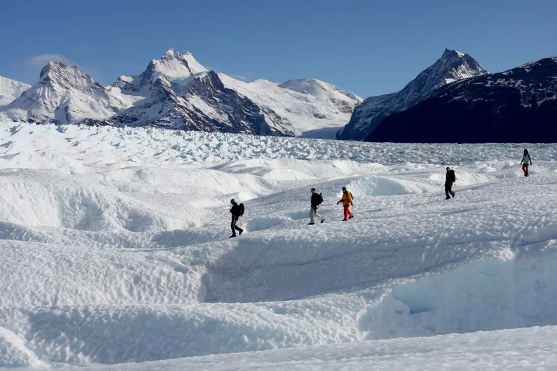 Walkers spread out across the glacier, with peaks behind them