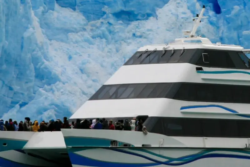 A catamaran full of passengers in front of the ice wall