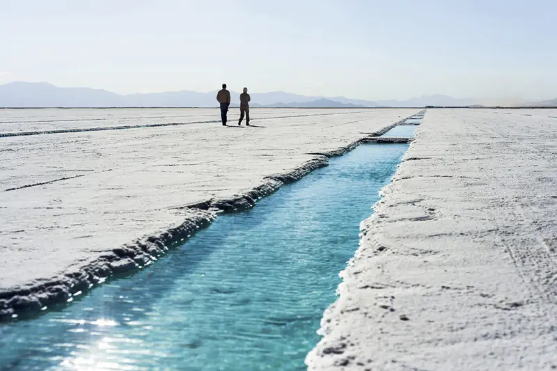 Two people walking on the salt flat beside a channel of water