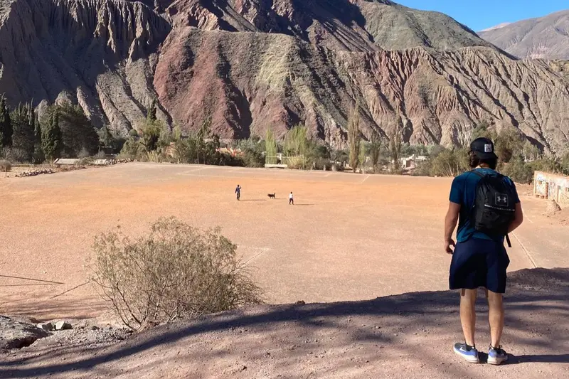 A walker on the desert floor below a wall of banded rock
