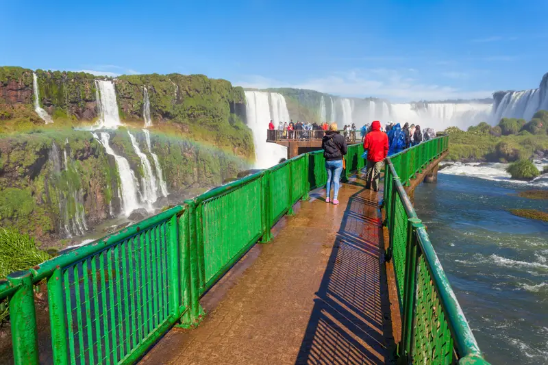 The green walkway on the Brazilian side, with the falls and a rainbow behind
