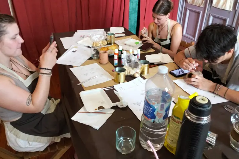People painting at a long table, with paints and sketches in front of them