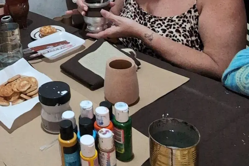 A table with a mate cup, jars of paint and brushes