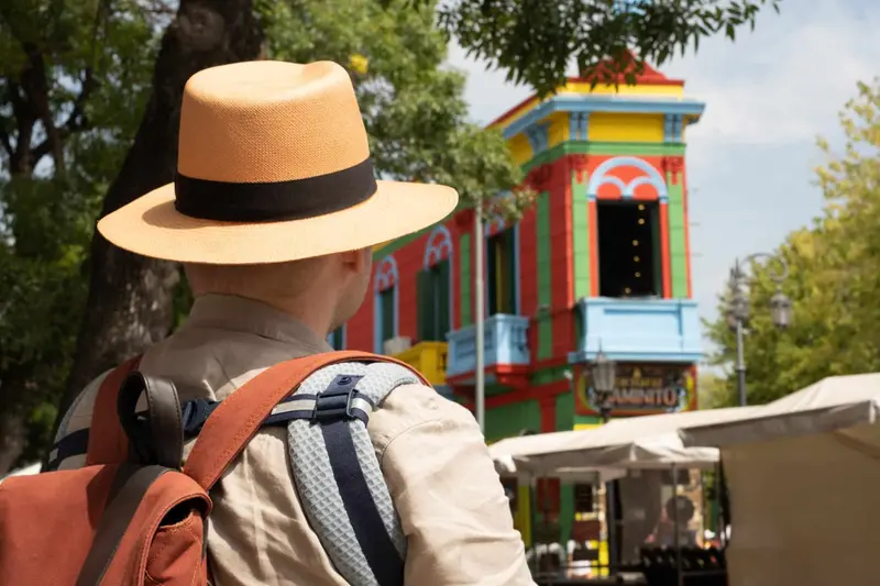 A visitor in a straw hat in front of the painted houses of Caminito