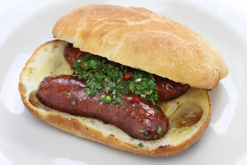 A choripán, sausage in a bread roll with chimichurri