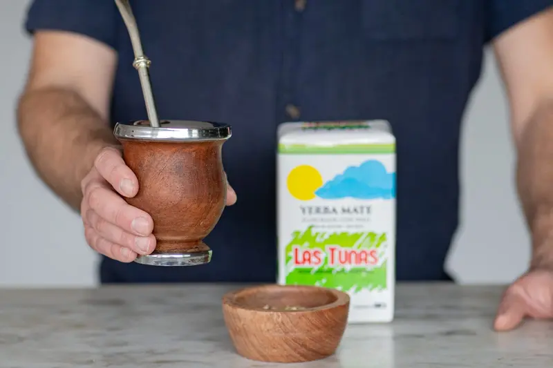 A hand holding a mate gourd beside a packet of yerba