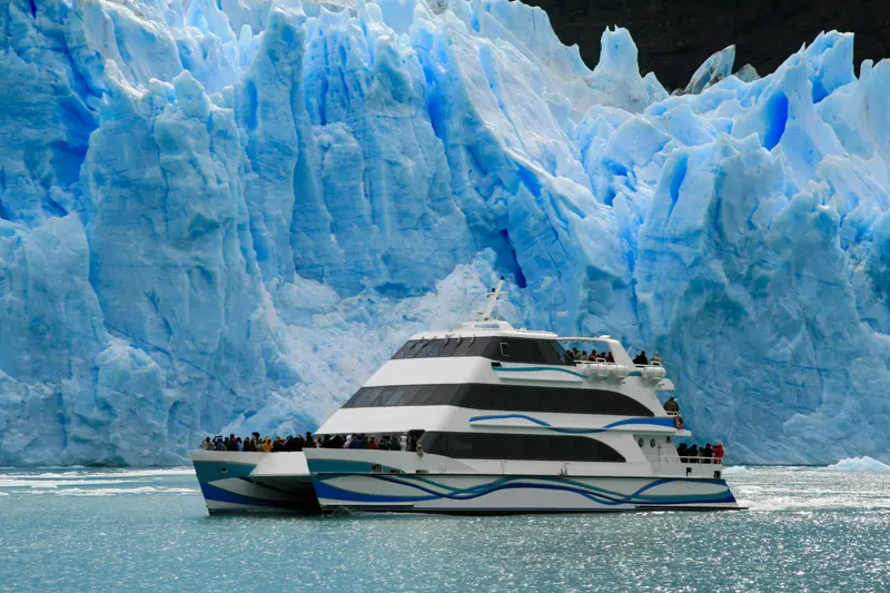 A catamaran in front of the wall of the glacier