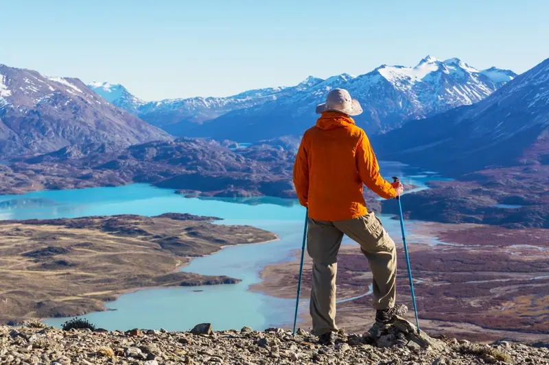 A walker with poles standing above a turquoise lake