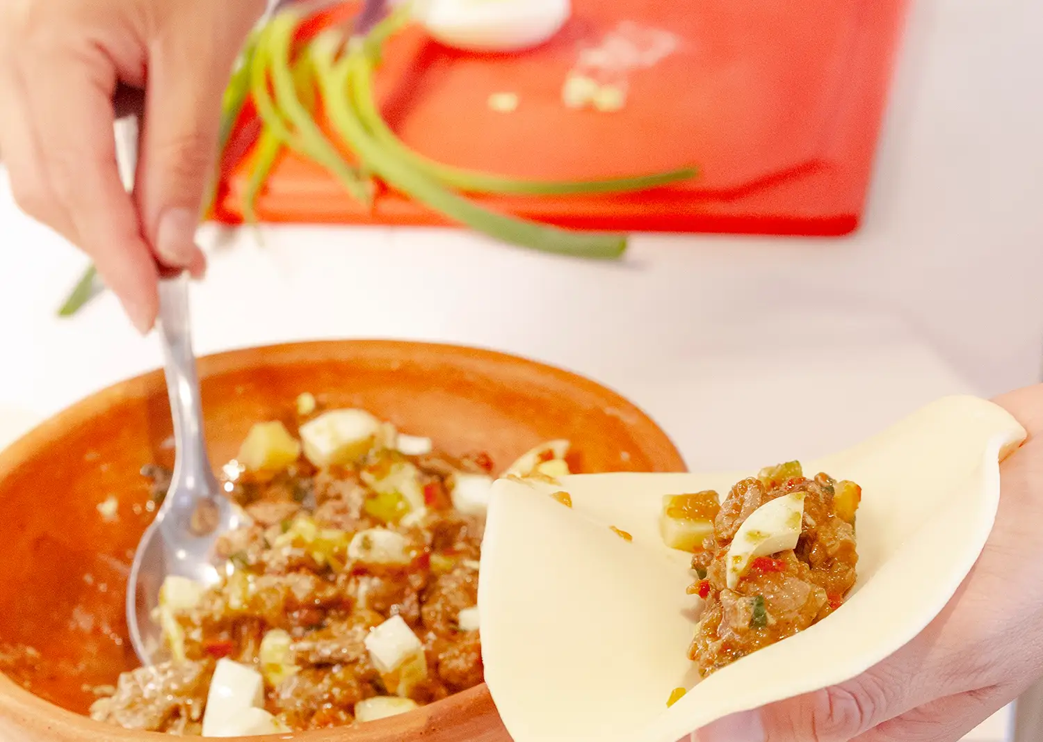A spoon over the bowl of filling, with a pastry disc and a folded empanada