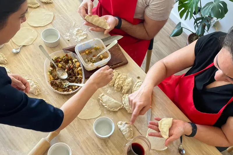 Hands folding empanadas at a table, with the filling in a dish