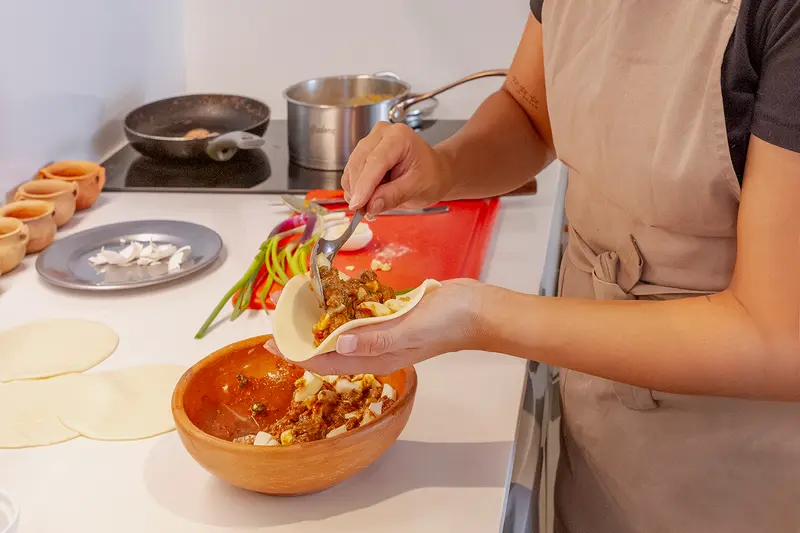 Hands filling a dough round at the stove