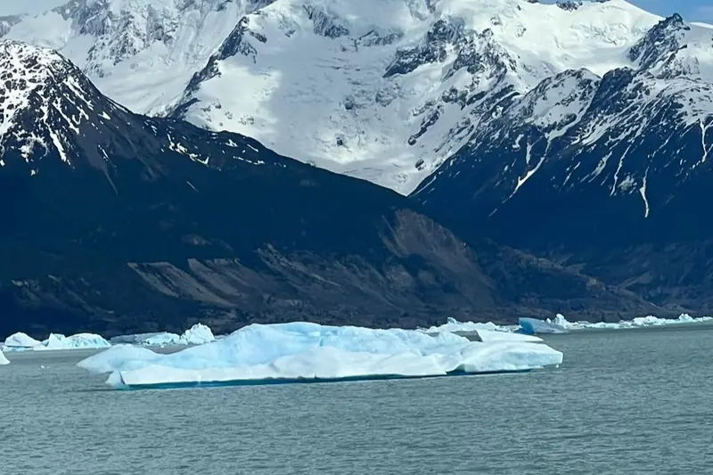 An iceberg on the lake with snow peaks behind it