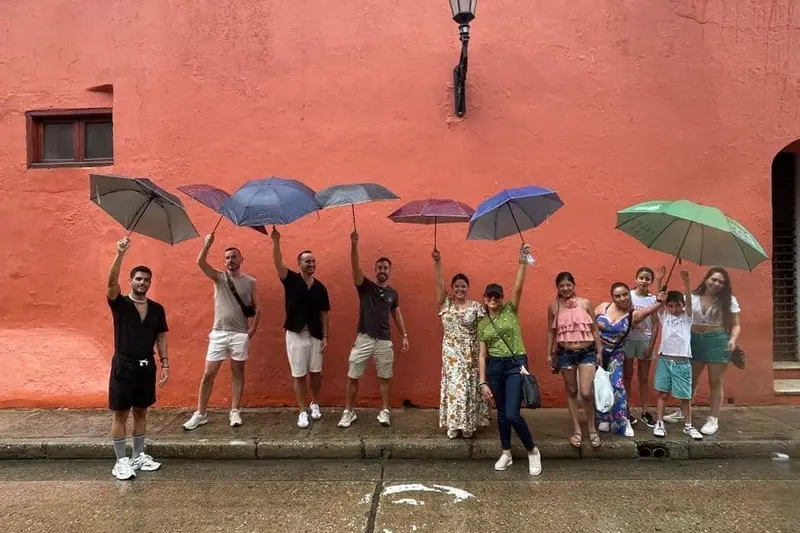A group with umbrellas raised against a red wall