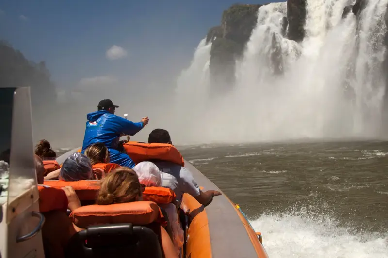 A boat of passengers in life jackets at the foot of a waterfall