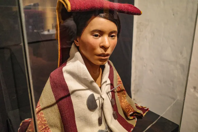 A figure in a woven mantle and red headdress in the museum display