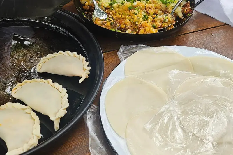 Folded empanadas on a tray beside the rolled dough discs