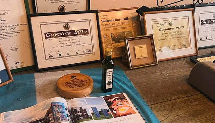 A table with framed awards behind a bottle of olive oil