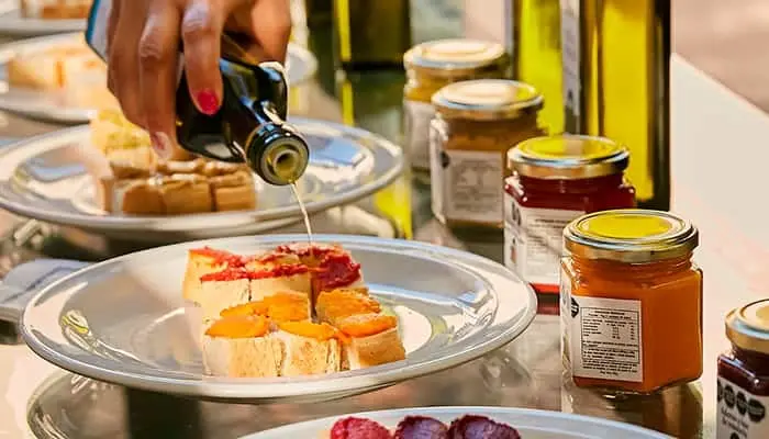 Olive oil being poured over toast, with jars alongside