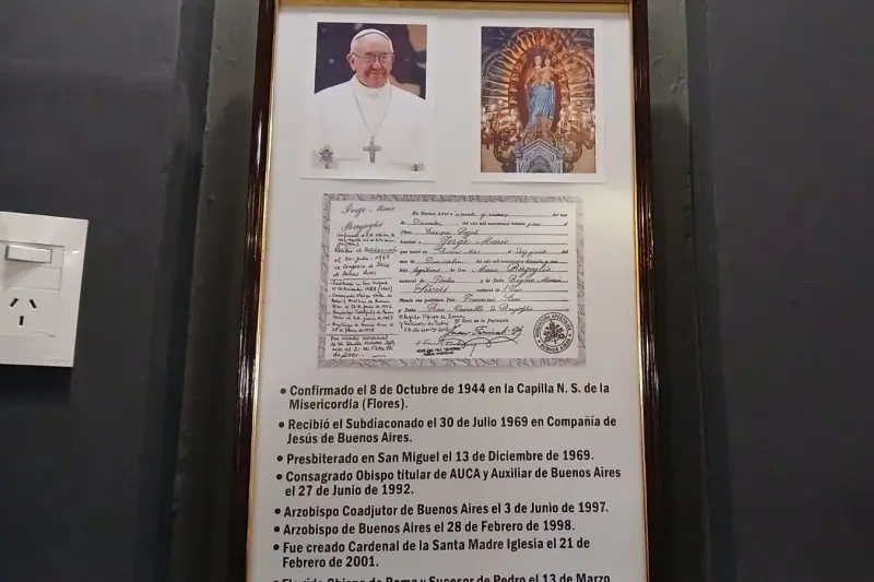 A framed record on a wall beside a portrait of Pope Francis