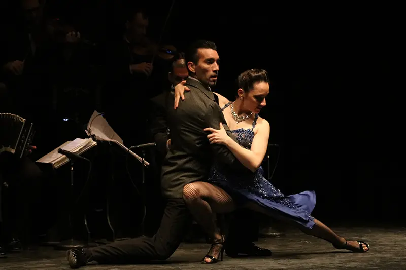 A tango couple mid-step on a dark stage