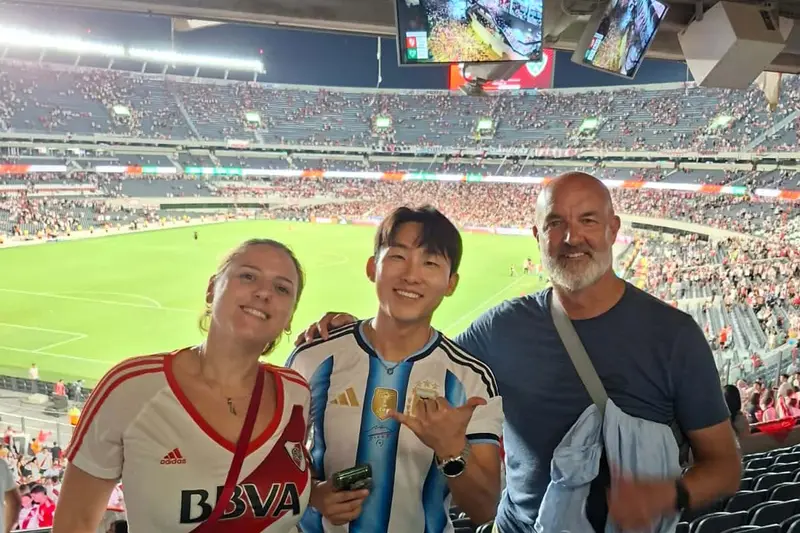 Three people in the stands with the pitch behind them