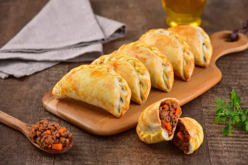 Empanadas on a board, one of them cut open to show the filling