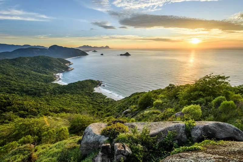 Green hills above the coast at sunrise, with rocks in the foreground