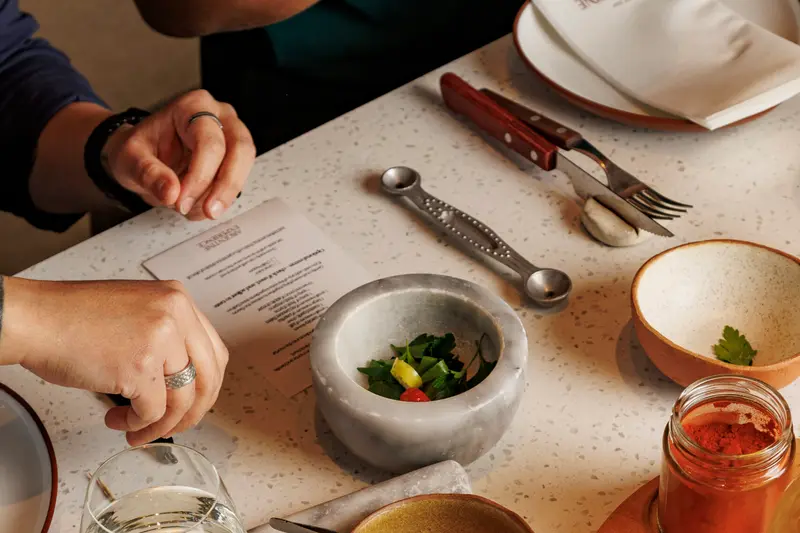 Hands at a laid table, with the menu, a mortar and small bowls