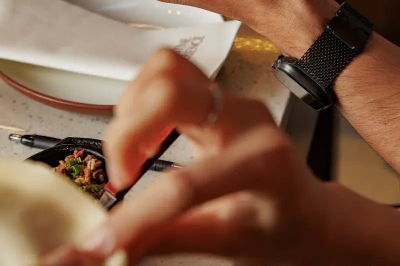 A hand serving over a plate, with a bottle of wine on the table