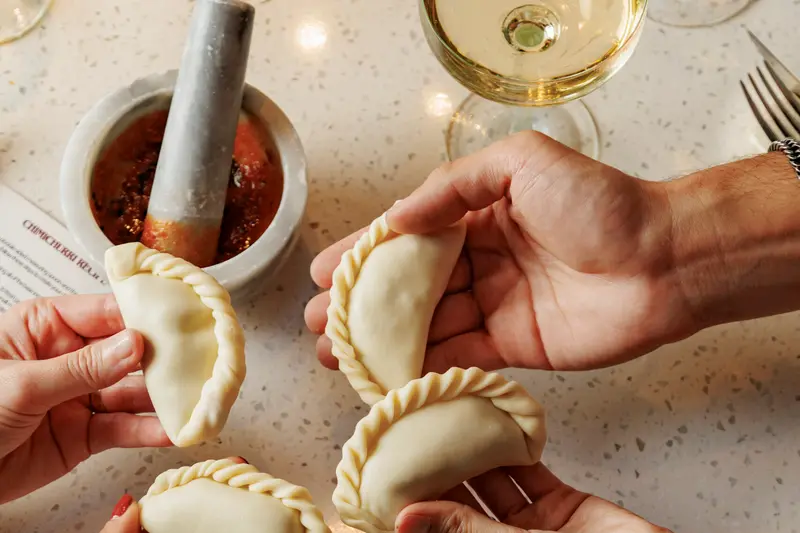 Two pairs of hands holding folded empanadas