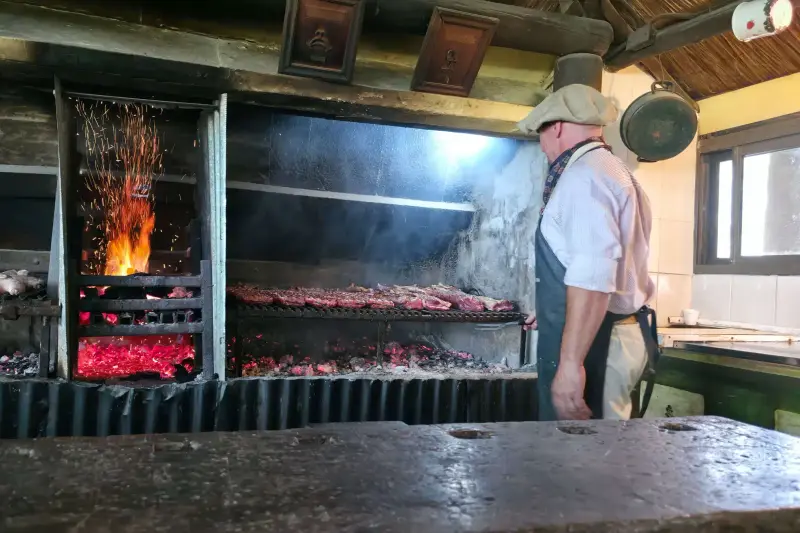 Meat on the asado grill over the coals, with the cook beside it