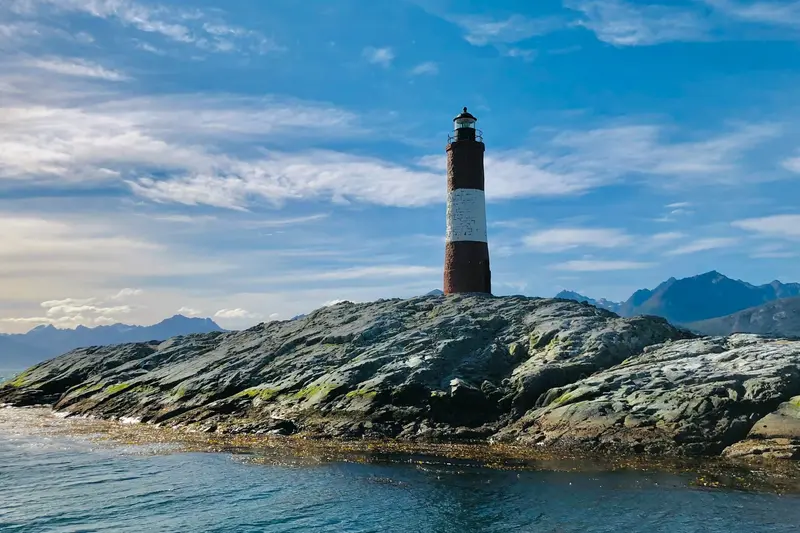 A black and white lighthouse on the rocks, with the mountains behind