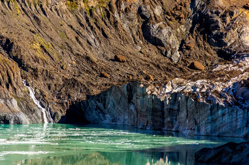 A waterfall running down a dark rock face into green water