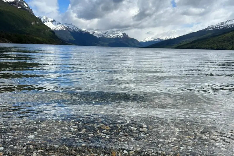 The shallow shoreline of the lake, with the snow range behind